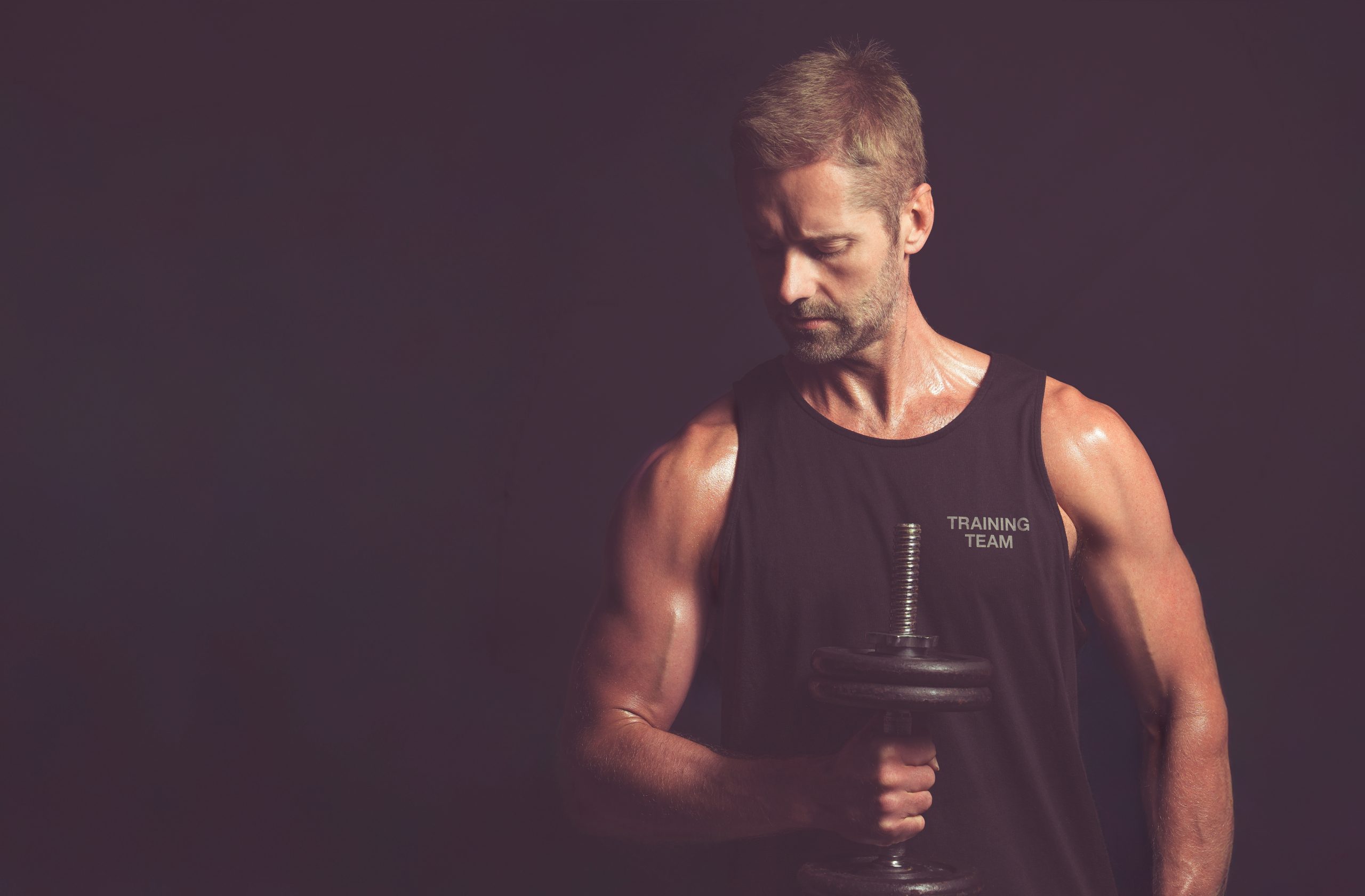 Fitness guides to get you moving, a lean man is lifting weights, covered in sweat in an atmospheric room